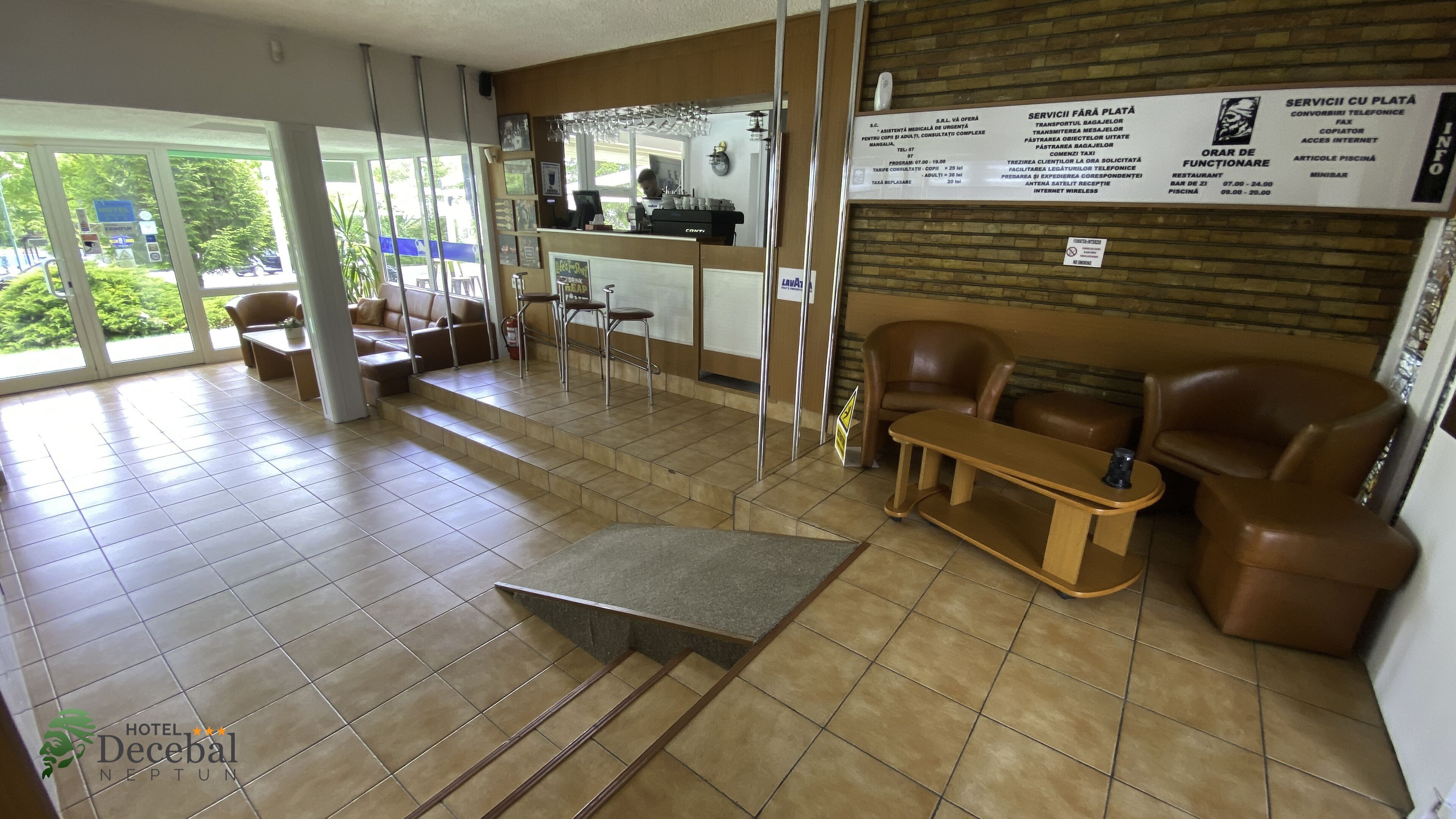 Vestíbulo de hotel con mostrador de recepción, zona de estar y vistas al exterior.
