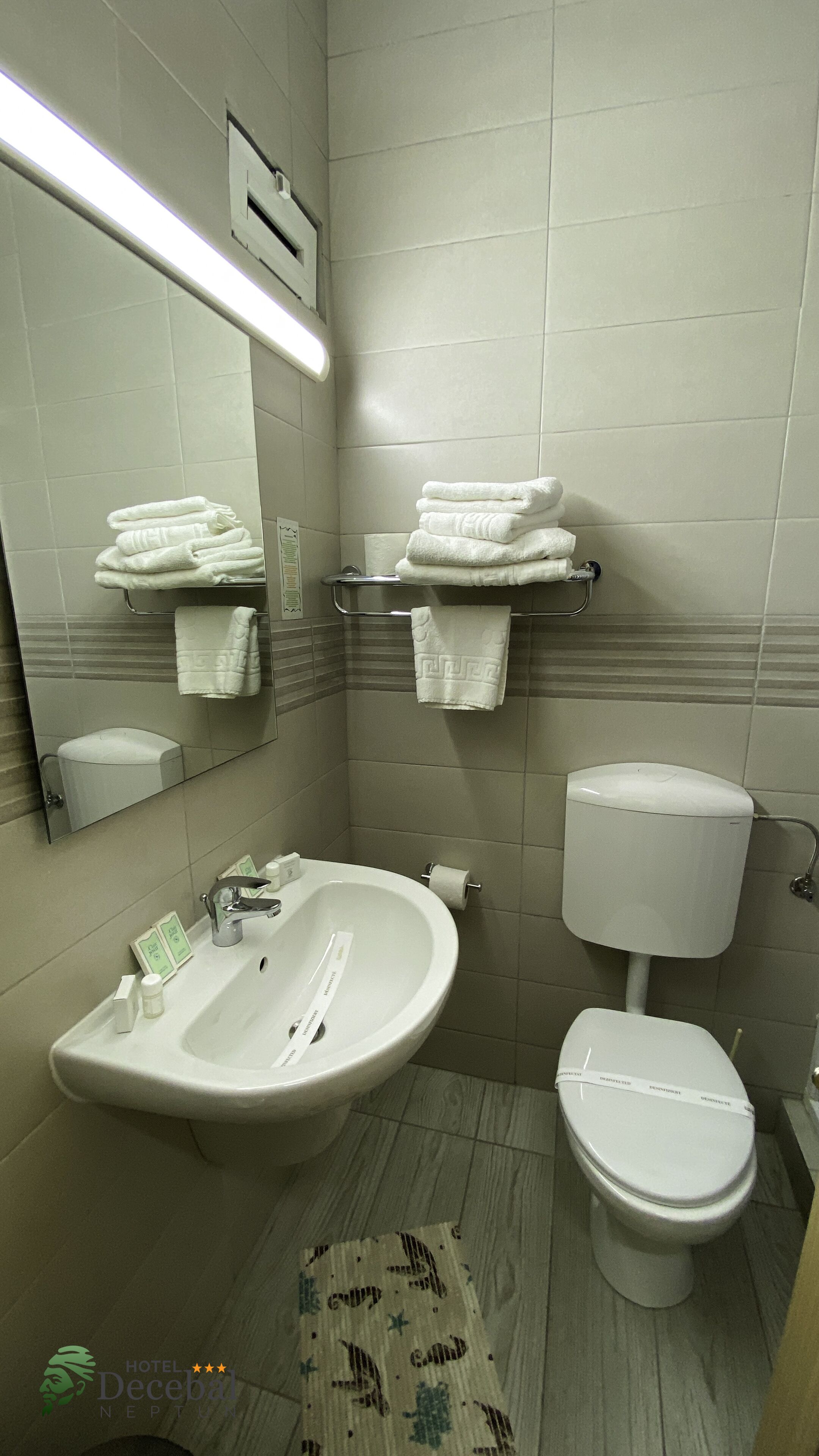 A bathroom with a sink, toilet, and a mirror. There are towels stacked on a rack.