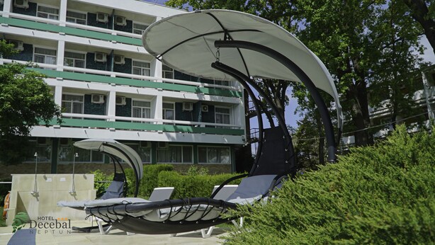 A hotel with outdoor seating under large umbrellas, a building with multiple floors, and greenery in the background. - Hotel Decebal Neptun (Neptun)