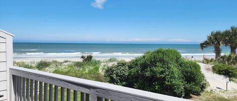 A wooden deck with a view of the beach and ocean.