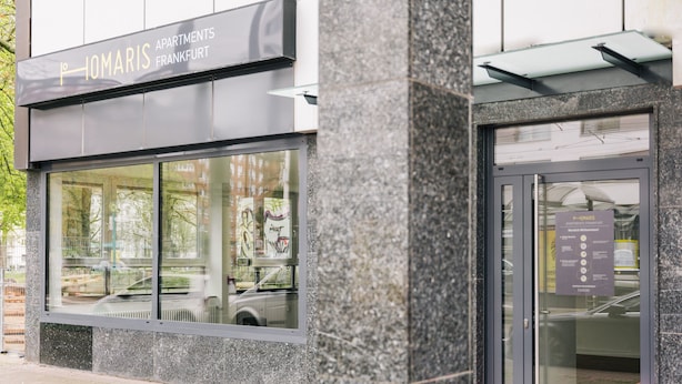 Un immeuble avec une enseigne indiquant « IOMARIS APARTMENTS FRANKFURT » et une entrée avec une porte en verre.