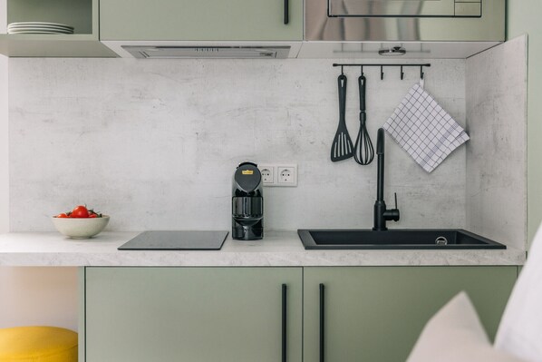 A kitchen with a marble countertop, a coffee maker, a sink, and green cabinets.