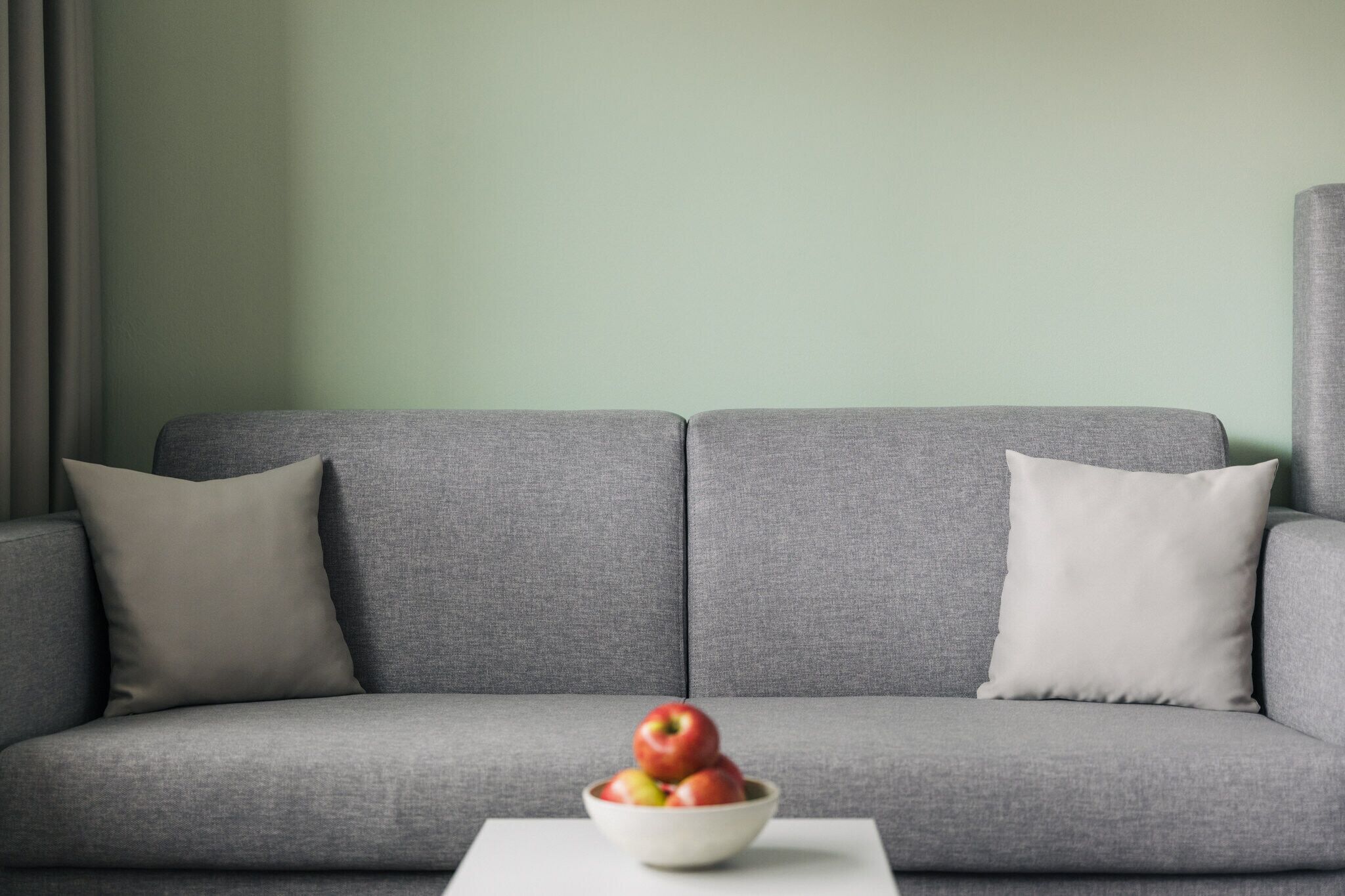 A grey sofa with a bowl of apples on a white table in front.