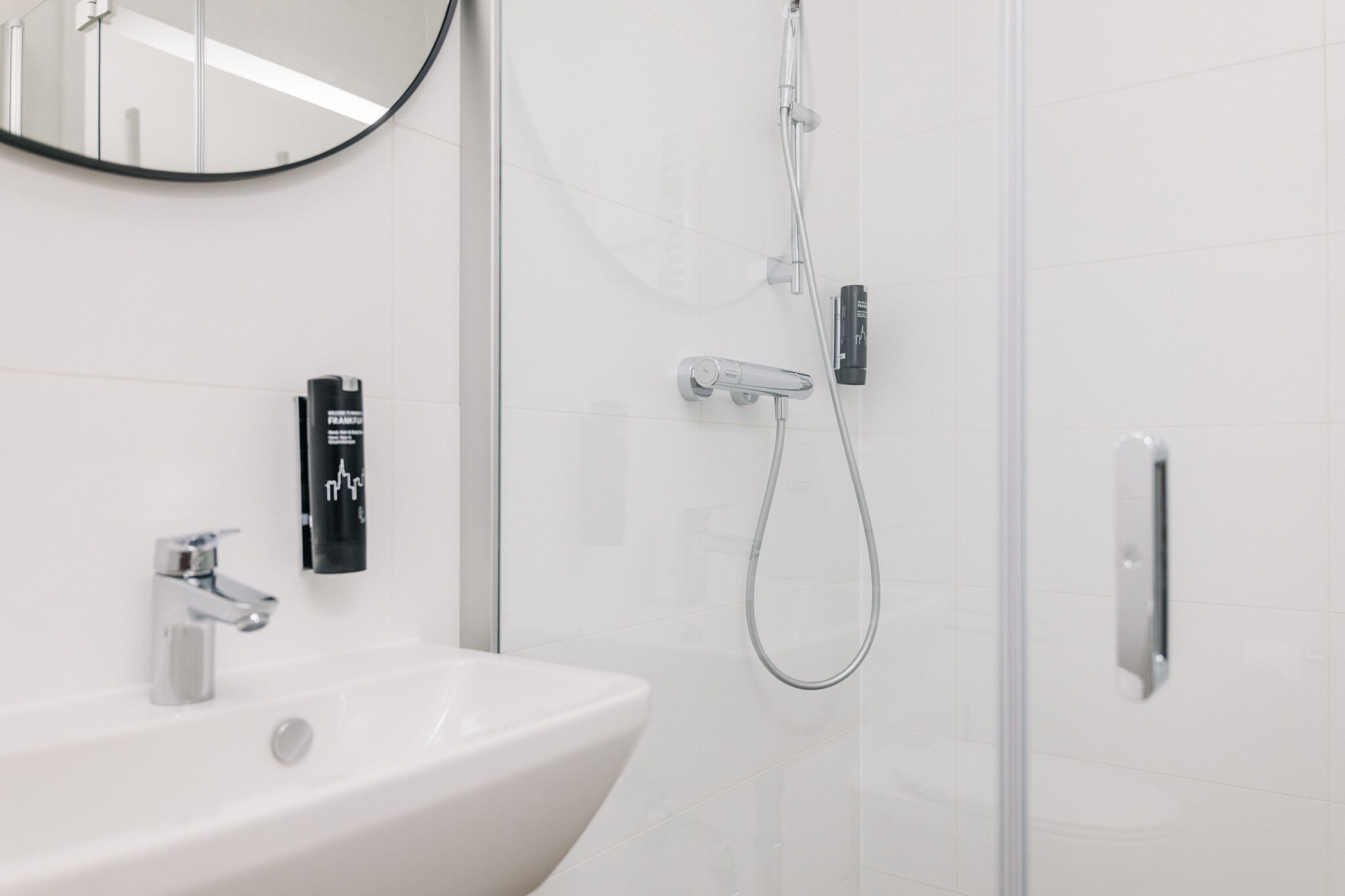 Een moderne badkamer met een wit wastafelmeubel, een handdouche en een douche met glazen wanden.