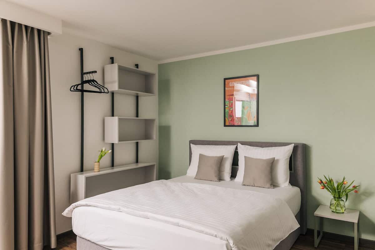 Ein ordentlich eingerichtetes Hotelzimmer mit Bett, Nachttischen, einem Wandregal und einem gerahmten Bild.