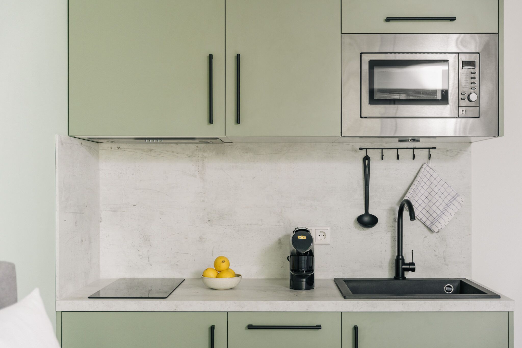 Una cocina con microondas integrado, cafetera y un tazón de limones en la encimera.