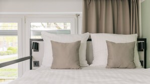 Un lit avec une literie blanche et deux oreillers beige, une tête de lit noire et une fenêtre avec des rideaux.