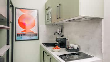Una cocina moderna con horno empotrado, cafetera y un bol con tomates en la encimera.