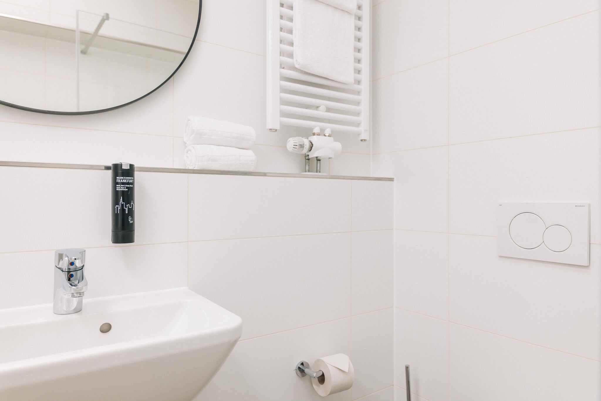 A modern bathroom with a white sink, a mirror, a towel rack, and a towel dispenser.