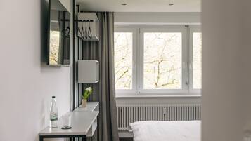 Ein modernes Hotelzimmer mit Bett, Schreibtisch mit Stuhl, Fenster mit Vorhängen und Heizkörper.