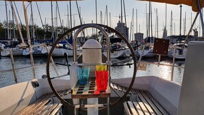 Ein Bootsdeck mit Steuerpult, einem kleinen Tisch mit Gläsern und Blick auf einen Jachthafen mit zahlreichen Booten.