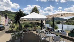 An outdoor seating area with tables and chairs under umbrellas, overlooking a body of water and hills. - Holiday on the Moselle in the Weinberg holiday apartment in Zell (Moselle) (Zell (Mosel))