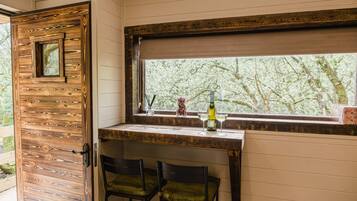 Una habitación con puerta de madera, ventana con vista a árboles, zona de bar con dos sillas y una botella en la encimera.