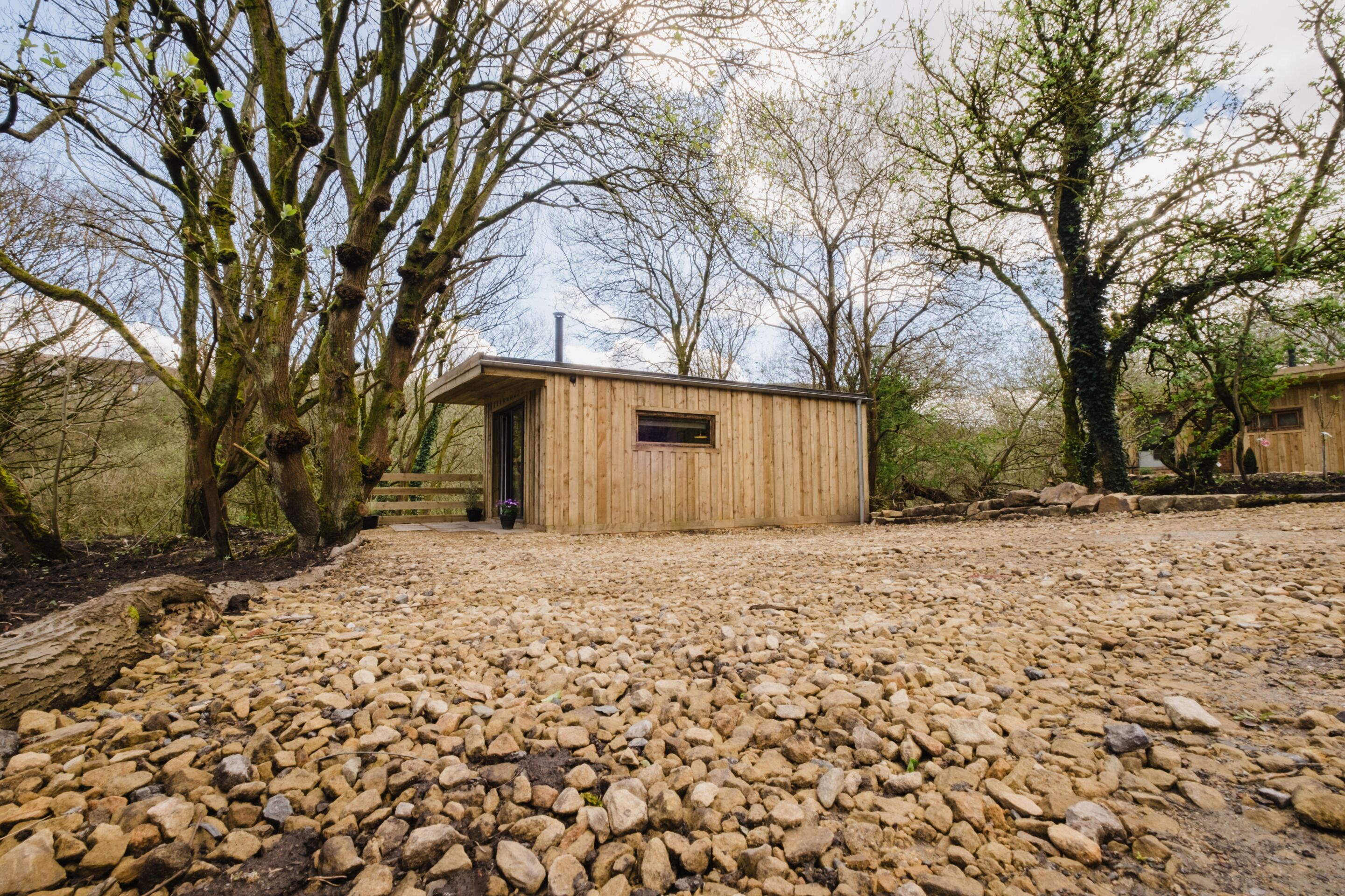 A wooden cabin with a gravel driveway, surrounded by trees.