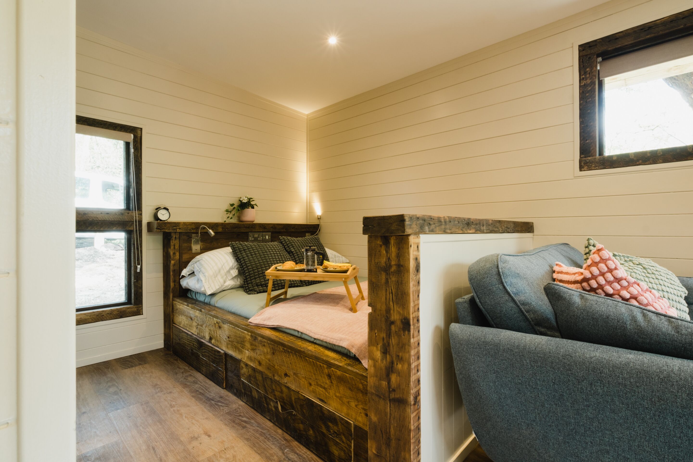 A cozy room with a wooden bed, a grey sofa, and a small table with a tray.