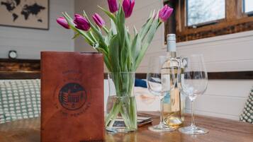 Un tavolo di legno con una borsa in pelle marrone, un vaso con tulipani viola e due bicchieri da vino vuoti.