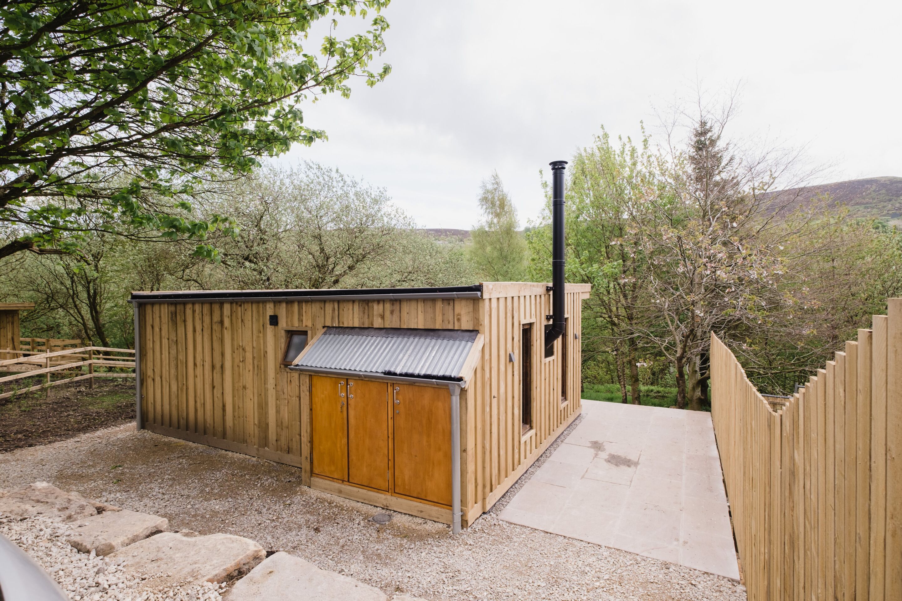 A wooden cabin with a metal roof, a chimney, and a gravel path leading to it.