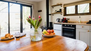 Une cuisine avec une table en bois, un vase de tulipes, un saladier de fruits et une machine à café.