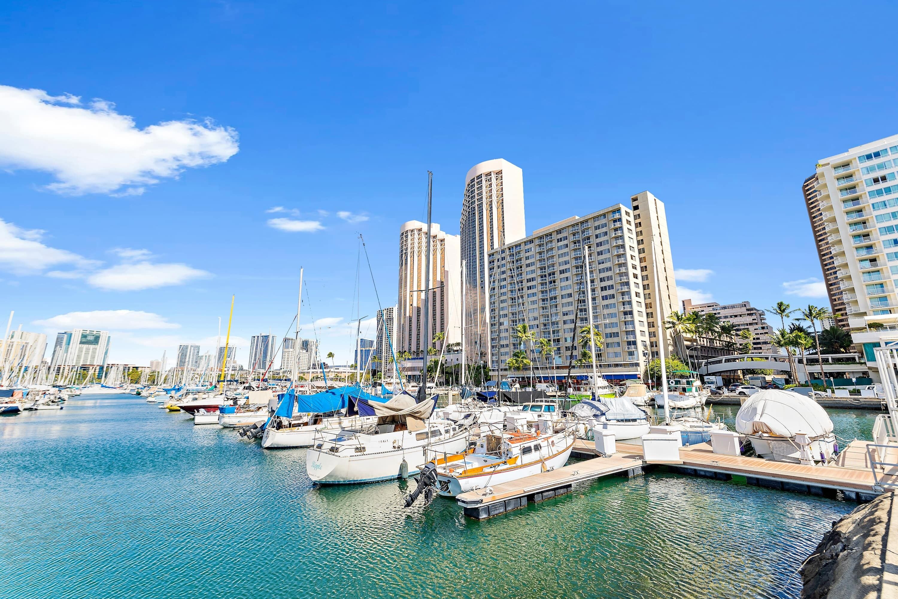 A marina with boats docked, surrounded by tall buildings and palm trees.