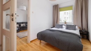 Un dormitorio con una cama grande, una ventana con cortinas, una puerta que da a otra habitación y una lámpara colgante.