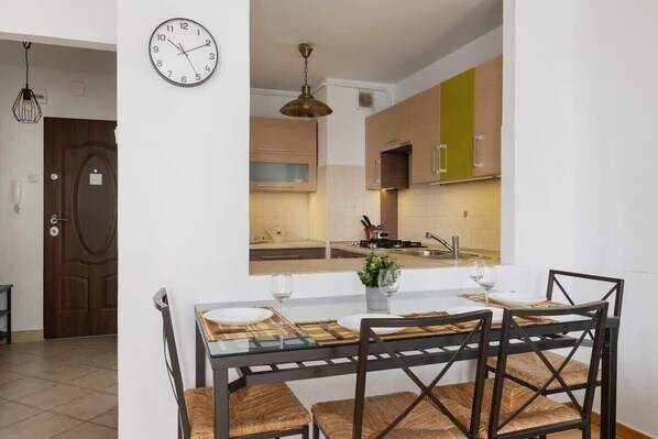 Una cocina moderna con una isla central, una zona de comedor con una mesa y sillas de vidrio, y un reloj visible en la pared.
