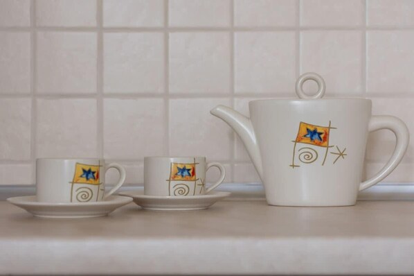 Una tetera blanca y dos tazas a juego con un diseño geométrico sobre una encimera de cocina.