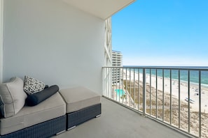 Un balcon avec un canapé, une vue sur la plage et un bâtiment en arrière-plan.
