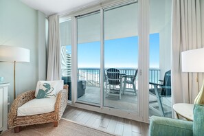 A room with a wicker chair, a table, and a view of the balcony.