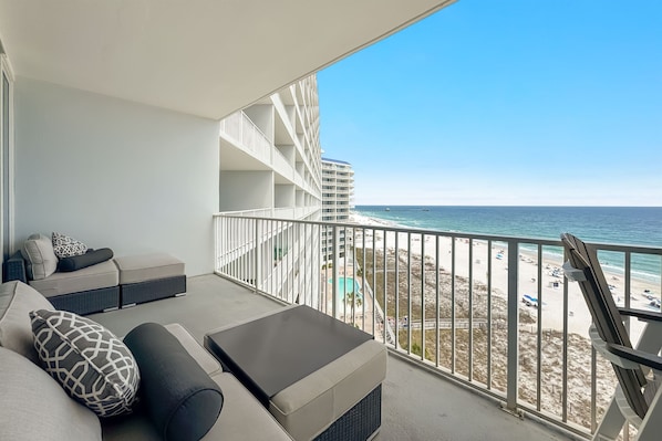 Un balcon avec vue sur la plage et l’océan, un canapé avec des coussins et une rambarde.