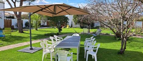 A patio with a table and chairs, a large umbrella, and a grassy area with trees.
