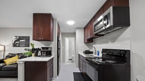 A modern kitchen with dark wooden cabinets, a stainless steel microwave, and a black stove. - Modern 1BD Apartment Near Ferndale (Hazel Park)