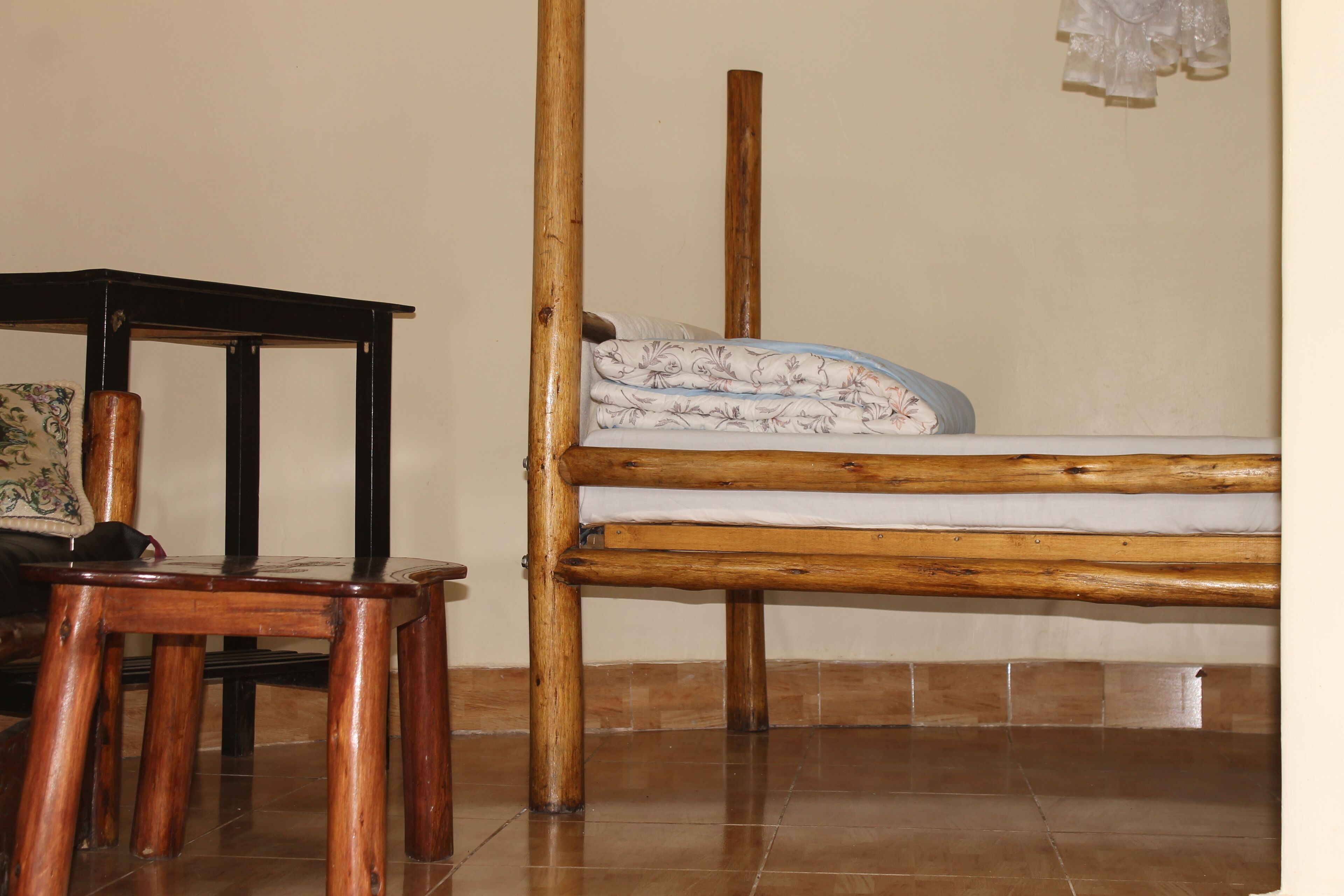 A room with a wooden bed, a small wooden table, and a tiled floor.
