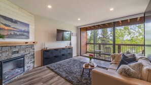 Een moderne woonkamer met een open haard, een bank, een salontafel en een groot raam met uitzicht op het landschap.