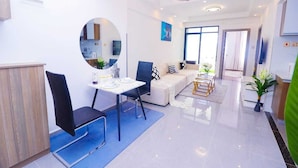 Ein modernes Wohnzimmer mit einer Couch, einem Esstisch und einem Couchtisch. Ein Fernseher ist an der Wand befestigt und ein Fenster sorgt für natürliches Licht.