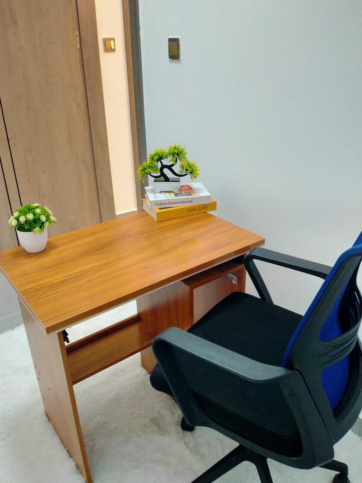 Een houten bureau met een zwarte kantoorstoel, een kleine potplant en een decoratief object op het bureau.