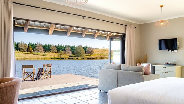 A bedroom with a large window, a bed, a TV, and a view of a lake and trees. - Springholm Cottages (Nottingham Road)