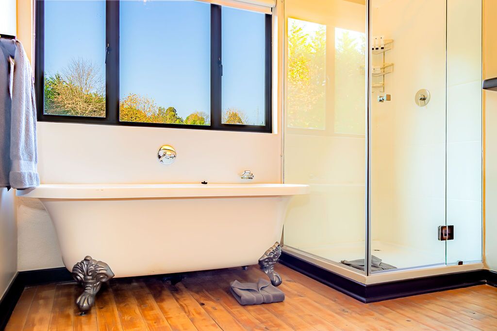 A modern bathroom with a freestanding bathtub, a glass shower enclosure, and a large window offering a view of trees.