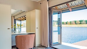 A room with a large sliding glass door leading to a pool, a white cabinet, a pink chair, and a vase with flowers. - Springholm Cottages (Nottingham Road)
