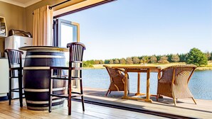 A wooden deck with a table and chairs, a large barrel, and a view of a lake. - Springholm Cottages (Nottingham Road)
