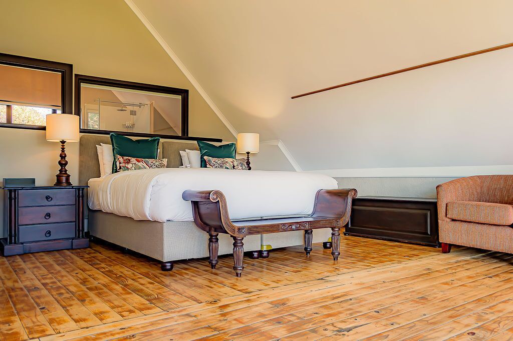 Un dormitorio con una cama grande, suelo de madera, una mesita de noche, una silla y una lámpara.