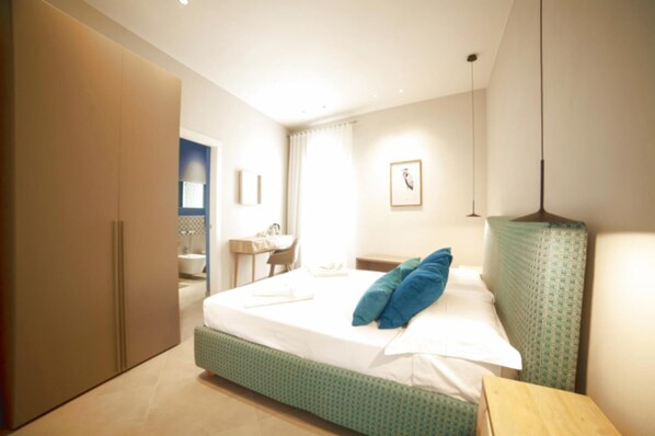 A modern bedroom with a bed, a desk, and a bathroom in the background.