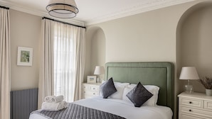 A neatly arranged hotel room with a large bed, two bedside tables with lamps, a radiator, and a window with curtains.