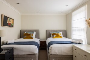 A hotel room with two beds, a nightstand, a dresser, and a window with sheer curtains.
