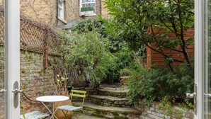 A small, enclosed garden area with a stone bench and table, surrounded by brick walls and lush greenery.