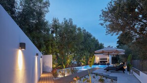 Zona de piscina exterior moderna amb un solàrium de fusta, envoltada per una paret blanca amb il·luminació integrada.