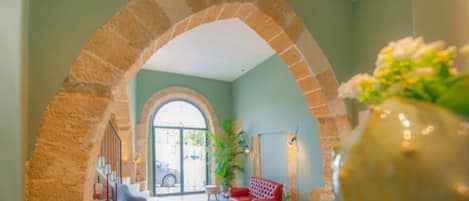 A lobby with a stone archway, a red sofa, a potted plant, and a view through a large arched doorway.