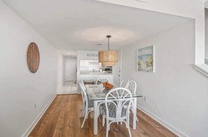 A dining area with a glass table and white chairs, a woven pendant light, and a wooden wall decoration. - 409 Captain John Fripp Villa (Fripp Island)