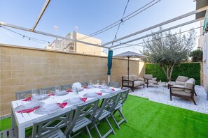 Un'area pranzo all'aperto con un tavolo apparecchiato per sei persone, circondato da sedie, e un'area relax con divani e un tavolino.