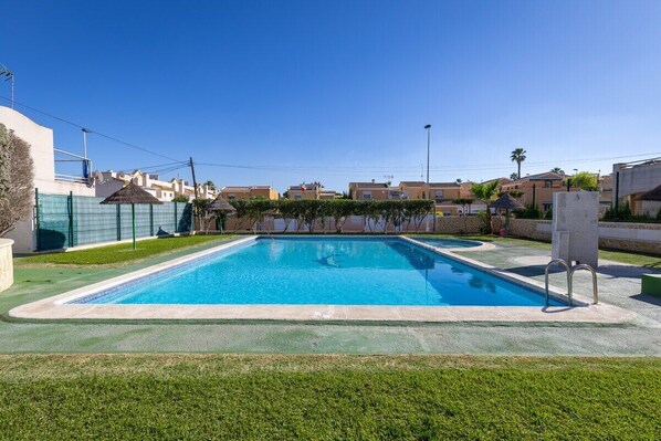 Une piscine rectangulaire à l’eau d’un bleu limpide, entourée d’une pelouse verdoyante et d’un petit muret en pierre.