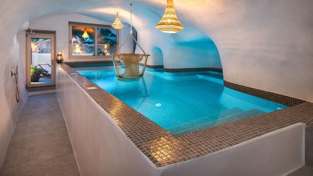 Una piscina interior con vistas despejadas al exterior, una silla de mimbre y dos lámparas colgantes.